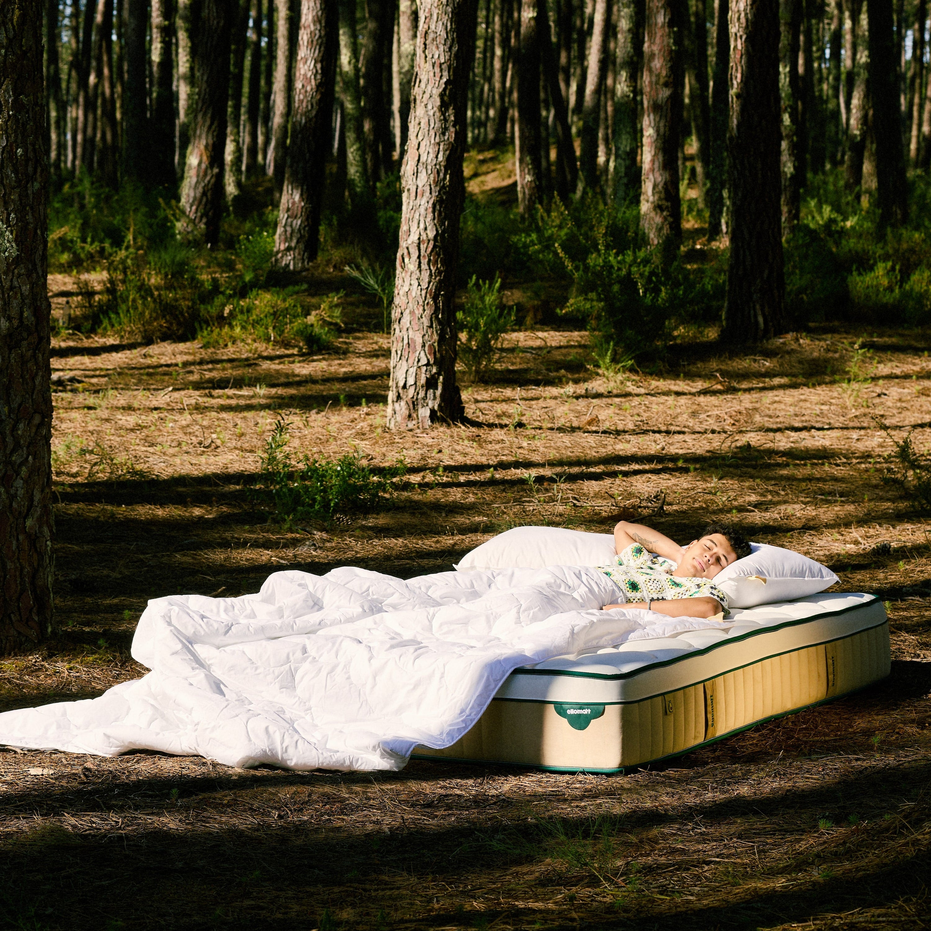 Person lying on a mattress outdoors in a forest