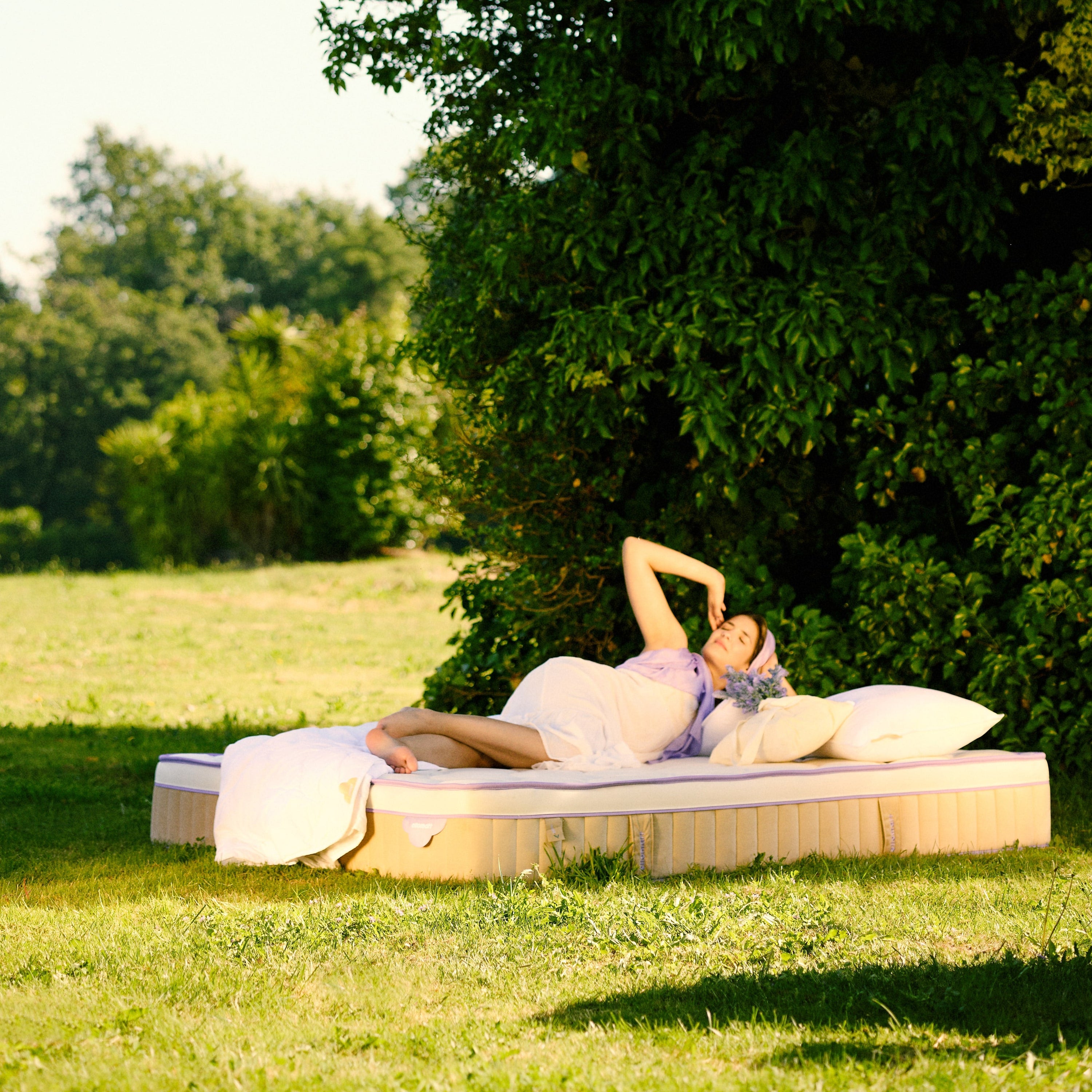 Person lying on a daybed in a grassy area with trees